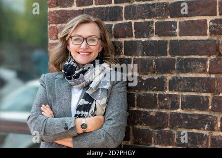 Portrait of a happy beautiful woman, 55 years old, smiling. On the street in the city, on the background of the old wall of red brick. Stock Photo