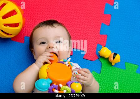 Funny baby playing on colorful eva rubber floor. Toddler having fun indoor his home. Top view. Copy space. Stock Photo