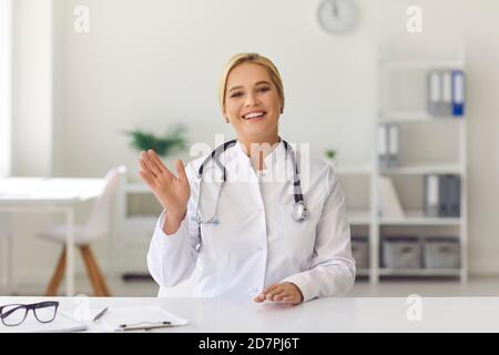 Smiling doctor waving hand starting video call with patient or recording medical vlog Stock Photo