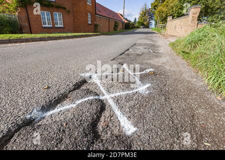 Pothole, pot holes in UK country road marked for highway maintenance Stock Photo