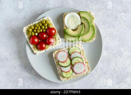 Homemade sandwiches with cherry tomatos, radish, cucumber, avocado and green pea on gray plate flat lay on light background. Slices of vegetables Stock Photo