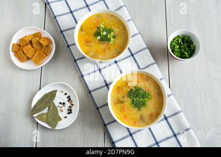 Noodle soup on a cotton napkin in two white bowls. Next to sliced green onions, crackers, spices. Delicious vegetarian food top view on a white wooden Stock Photo