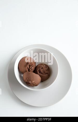 Three brown sponge cakes lie in a deep white plate. It stands on another flat, white plate. Flat lay, vertical composition with copy space on a white Stock Photo