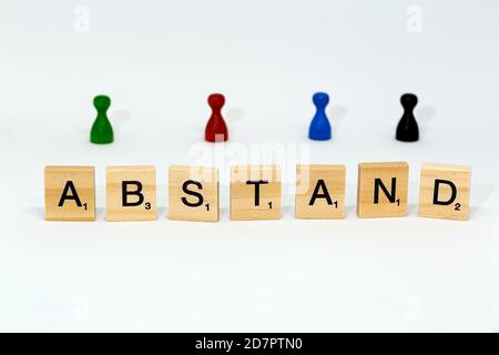 Letter blocks form the word 'Abstand' (distance), behind them colourful game pieces, symbolic image of the distance rule in the Corona crisis Stock Photo