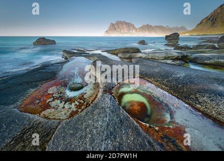 Rocks on the beach, in front tidal pond with formation Eye of Utakleiv, Nordland, Lofoten, Norway Stock Photo