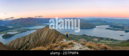 Young man standing on the summit, view of mountains and lake from Mount Roy, Roys Peak at sunset, Lake Wanaka, Southern Alps, Otago, South Island Stock Photo