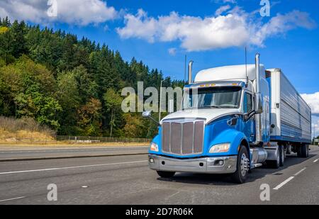 Blue and white big rig industrial grade bonnet long hauler diesel semi truck with refrigerator semi trailer running with commercial cargo on the wide Stock Photo