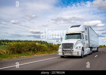 Powerful big rig white industrial grade high cab diesel semi truck with pipe grille guard transporting commercial cargo in dry van semi trailer runnin Stock Photo