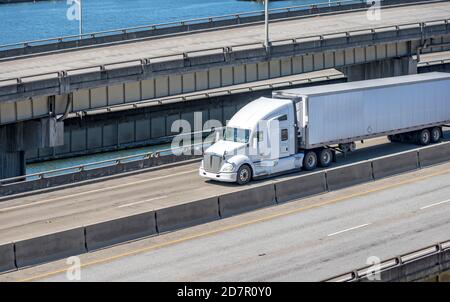 White bonnet industrial grade diesel big rig semi truck tractor transporting commercial cargo in refrigerated semi trailer running on the multilevel o Stock Photo
