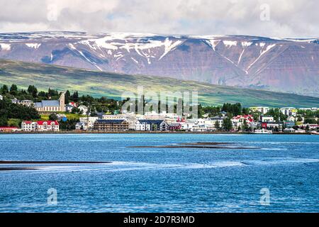 Akureyri, Iceland - June 17, 2018: Cityscape skyline view of town fishing village with fjord and snow covered mountain peak and houses buildings by wa Stock Photo