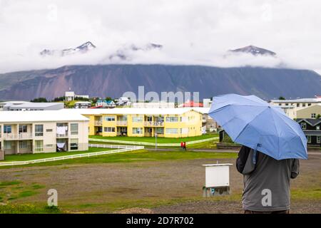 Hofn, Iceland closeup of man holding umbrella back looking at cityscape landscape view of peaceful small fishing village town in rain, raining weather Stock Photo