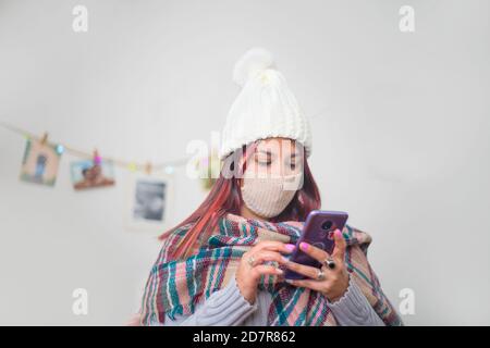 Hispanic woman dressed in warm clothes and a mask looking at her phone Stock Photo