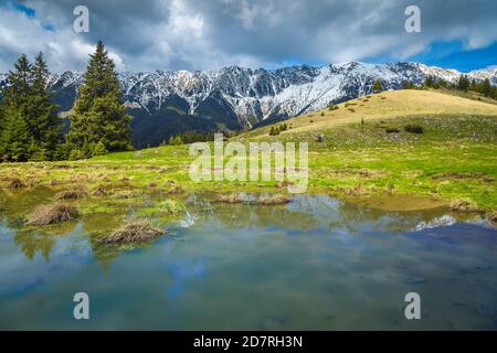 Amazing alpine landscape with small lake and high snowy Piatra Craiului mountains, near Pestera village, Transylvania, Romania, Europe Stock Photo