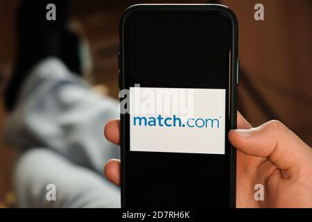 Match com logo on the screen of mobile phone in mans hand. Application for dating and acquaintance. Man is laying on the sofa and looking for partner Stock Photo