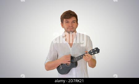 Young man playing ukulele while walking on gradient background. Stock Photo