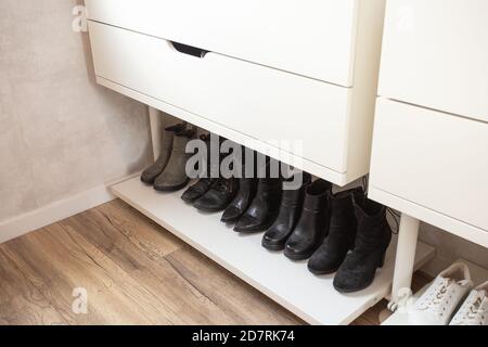 Organized shoe rack, shoe rack with black stylisch shoes and boots, on a wooden floor, besides a white wall. modern room Stock Photo