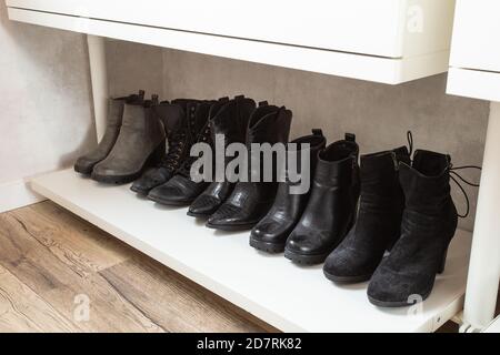 Organized shoe rack, shoe rack with black stylisch shoes and boots, on a wooden floor, besides a white wall. modern room Stock Photo