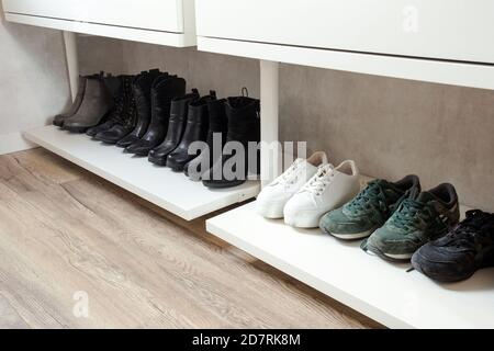 Organized shoe rack, shoe rack with black stylisch shoes and boots, on a wooden floor, besides a white wall. modern room Stock Photo