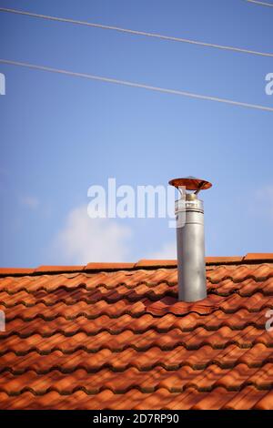 Red tile roof with galvanized chimney chimney against blue sky Stock Photo