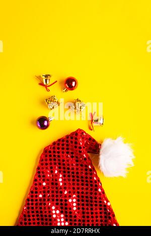 Santa Claus hat with christmas balls, gifts and sparkling bells on a yellow background. Stock Photo