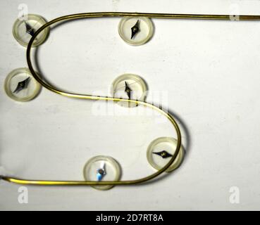 Magnetic field around a conductor. The compass needles align to the field generated by the current, rather than the geomagnetic poles. Black on the co Stock Photo