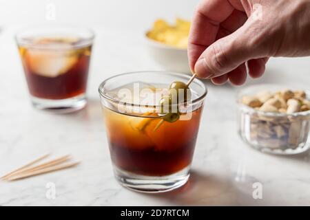 Man's hand picking olives from red vermouth Stock Photo