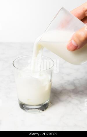Man's hand pouring fresh milk into a glass with ice cubes. Dalgona coffee preparation Stock Photo