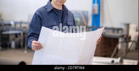 Blue dressed engineer reading a bluepring drawing in an industrial facility. Face not visible Stock Photo