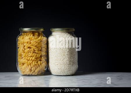 Set of glass jars with pasta and rice placed on a marble tabletop. Zero waste concept Stock Photo