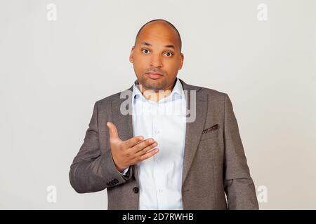 Young african american guy businessman looking at the camera with a surprised facial expression and gesturing with his hand. Standing on a gray background Stock Photo
