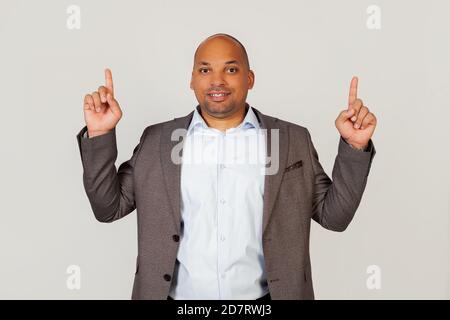 Young african american guy businessman looking at the camera laughing and pointing up with both hands and forefingers. Copy ad space. Copy space. Standing on a gray background Stock Photo