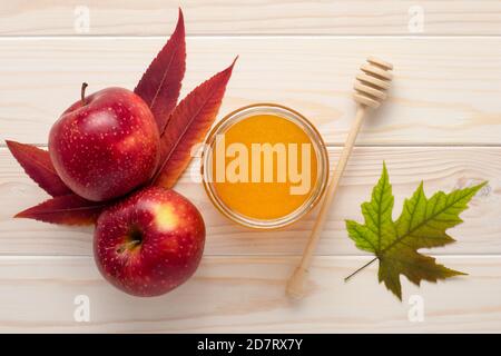 Honey in a glass jar and red apples on a white wooden background. Celebration Rosh Hashanah, full year bliss. Autumn season, fall leaves. Harvest conc Stock Photo