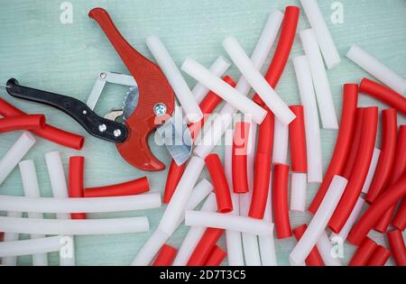 Red and white pvc pipes for warm floor. Scissors for plumbing on wooden background. Stock Photo