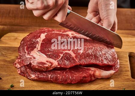 Chef cutting beef meat with Santoku knife on wooden cutting board Stock Photo