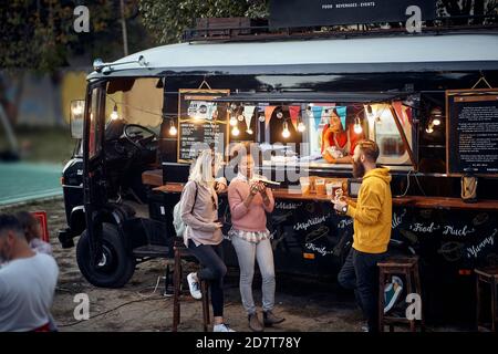 group of friends eating, drinking, talking, socializing outdoor in front of modifed truck for fast food service Stock Photo
