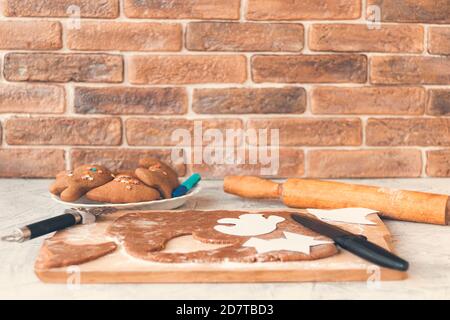 Preparation for Halloween.Making homemade gingerbread cookies for Halloween on brick wall background.Halloween gingerbread. Cutting out gingerbread Halloween. Soft focus. Copy space Stock Photo