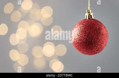Red sparkling Christmas tree decoration against blurred lights on gray background. Stock Photo