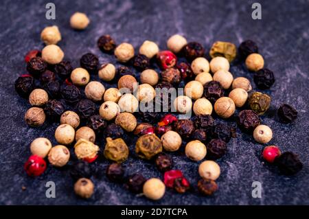 Close-up of 4 kinds of peppercorns on a dark textured surface Stock Photo