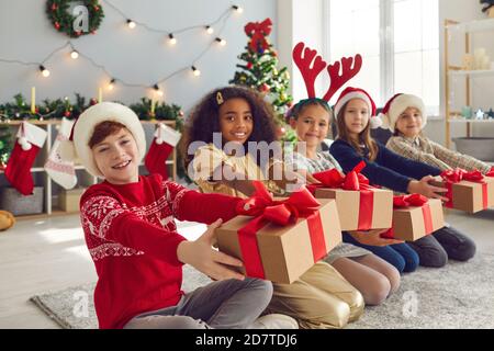 Group of happy smiling children sitting in row in living-room and holding Christmas presents Stock Photo