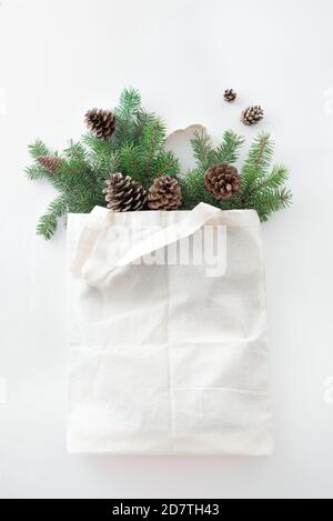 Christmas composition. Eco bag with Christmas tree branches and pine cones on white background. Christmas coming and gift delivery concept. Top view, Stock Photo