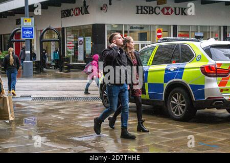 A couple (man and woman) walk past a police car during a rainy day in Birmingham, UK Stock Photo