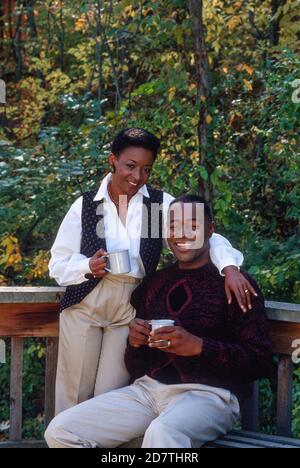 african american handsome husband and wife sitting on bed, holding ...