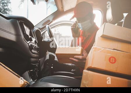 Delivery man call to customers services and wearing medical mask for safety protection from virus infection sender working with postal boxes on Stock Photo