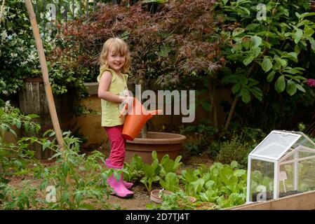 Three year old girl watering plants in the garden. Stock Photo