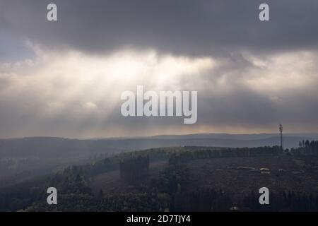 Beautiful view of the forest on hills gleaming under the sunrays piercing through the clouds Stock Photo