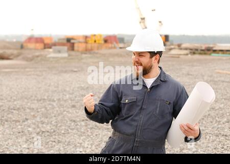 Happy building engineer holding blueprints papers on construction site. Stock Photo