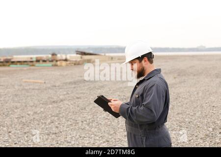 Foreman in helmet surfing internet by tablet on construction site. Stock Photo