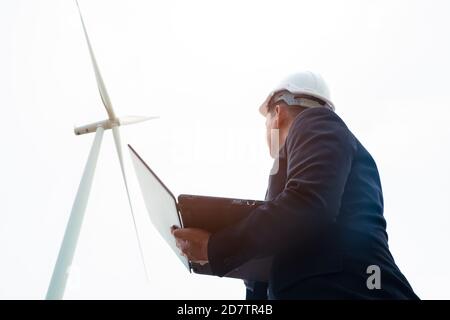 Engineers windmills are working on laptop with the wind turbine in background Stock Photo
