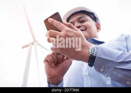 Engineers windmills are working on smartphone with the wind turbine in background Stock Photo