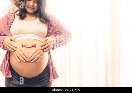 Pregnant couple of husband and wife feels love and relax at home. Young expecting woman holds baby in pregnant belly. Father take care of pregnant Stock Photo